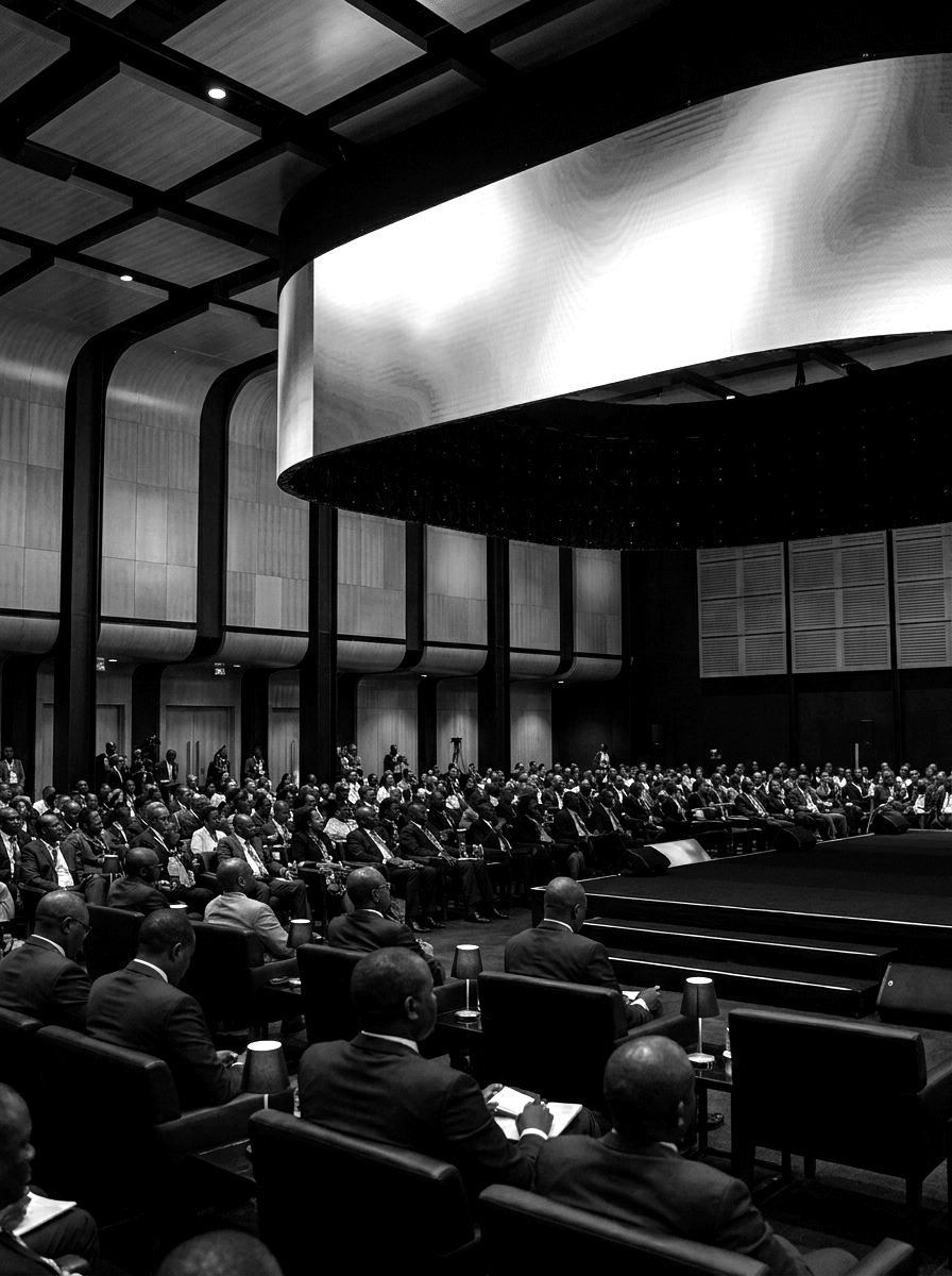 A conference auditorium with a vast curved screen above a full hall of delegates